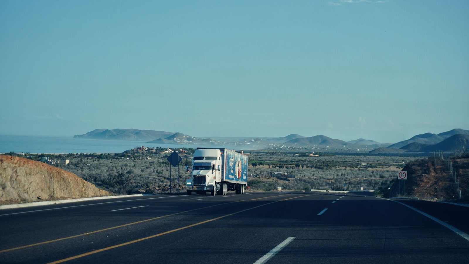 Semi truck cresting a highway with hills and sea on the horizon